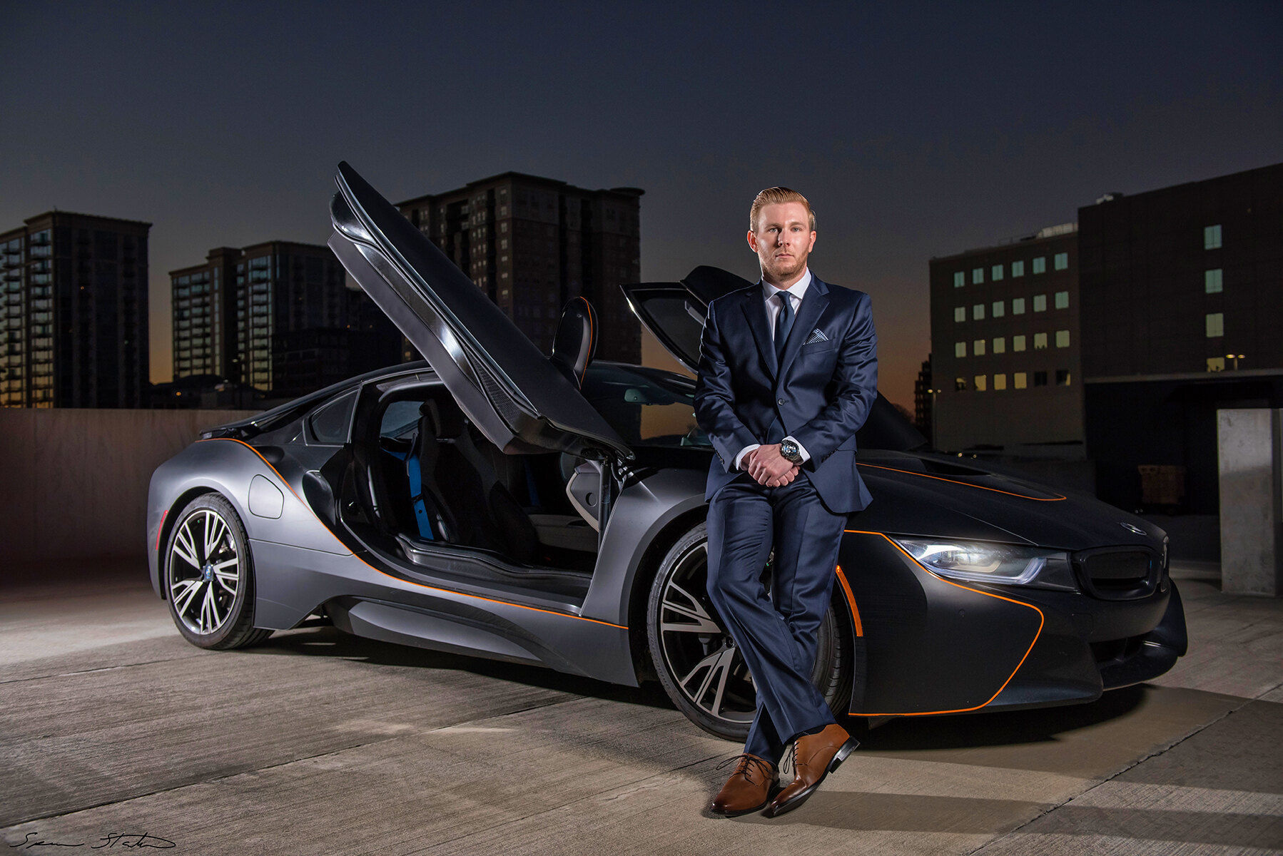 Entrepreneur Ryan White, founder of Social Revelation, sitting on the front of a BMW i8 on a city rooftop at dusk